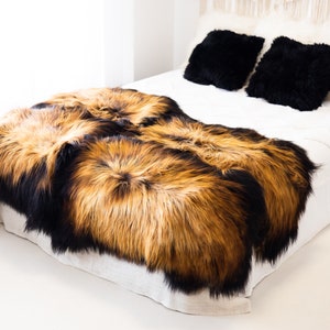 May include: Two sheepskin throws in black and brown tones, arranged on a white bed with black and white pillows. The throws are soft and fluffy, and would be perfect for adding warmth and texture to any room.