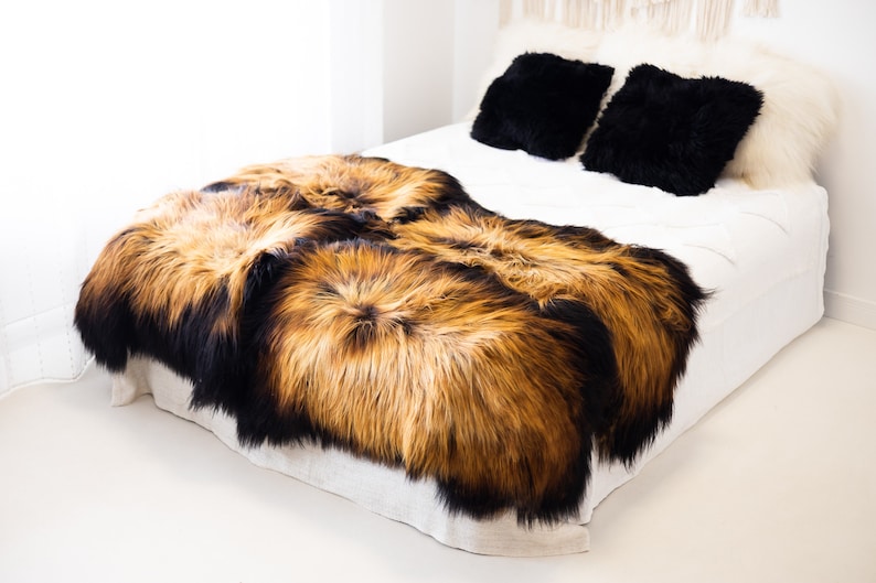 May include: Two sheepskin throws in black and brown tones, arranged on a white bed with black and white pillows. The throws are soft and fluffy, and would be perfect for adding warmth and texture to any room.