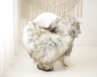 May include: A white rocking chair with a fluffy gray and white sheepskin throw draped over it.