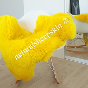 May include: A bright yellow sheepskin rug draped over a white rocking chair. The rug is soft and fluffy, and the chair is made of metal and wood. The text "naturalsheepskin &copy;" is visible on the rug.