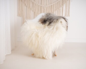 May include: A white and gray sheepskin rug draped over a white chair. The rug is fluffy and soft, and the chair is modern and stylish.