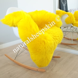 May include: A bright yellow sheepskin rug draped over a white rocking chair. The rug is soft and fluffy, and the chair is made of metal and wood. The text "naturalsheepskin" is visible on the rug.