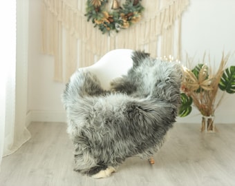 May include: A white chair with a gray and white faux fur throw draped over it. The chair is in a room with a white wall and a white curtain.