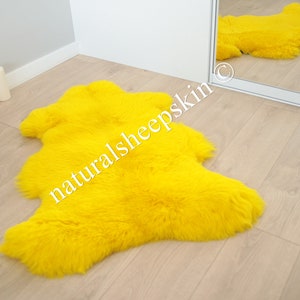 May include: A bright yellow sheepskin rug with long, fluffy fur. The rug is laid out on a light wood floor.