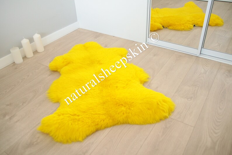 May include: A bright yellow sheepskin rug with long, fluffy fur. The rug is laid out on a light wood floor.