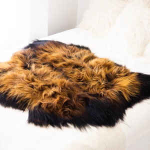 May include: A brown and black sheepskin rug with long, soft fur. The rug is laid out on a white bedspread.