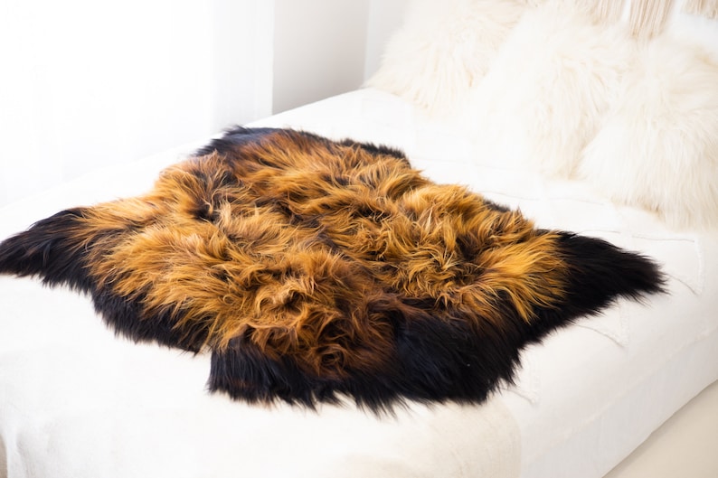 May include: A brown and black sheepskin rug with long, soft fur. The rug is laid out on a white bedspread.