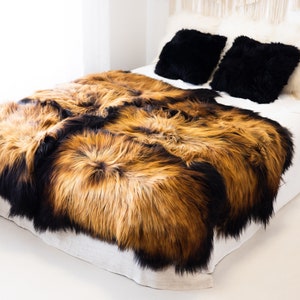 May include: A brown and black sheepskin rug with long fur is placed on a white bed with black and white pillows.