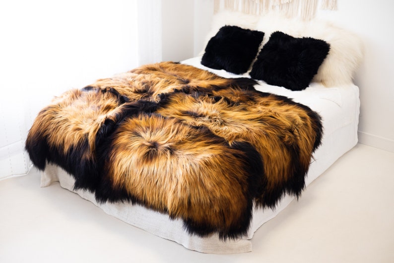 May include: A brown and black sheepskin rug with long fur is placed on a white bed with black and white pillows.