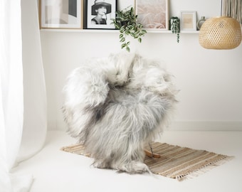 May include: A fluffy, light gray faux fur chair cover with a wooden base sits on a small, rectangular, woven rug. The chair cover has long, soft fur and is the focal point of the image. The rug has a natural, neutral color palette.