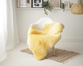 Può includere: Un tappeto di pelle di pecora giallo drappeggiato su una sedia bianca. Il tappeto è morbido e soffice, e la sedia è moderna ed elegante. Il tappeto è un'ottima aggiunta a qualsiasi arredamento domestico.