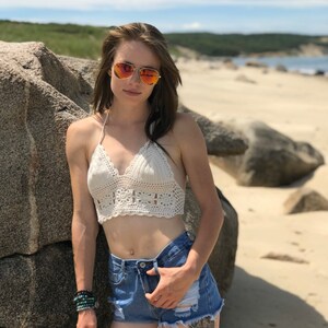 May include: A woman wearing a white crochet halter top and denim shorts with a wolf tattoo on her thigh. She is wearing sunglasses and has long brown hair.