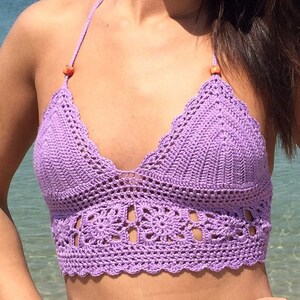 May include: A purple crochet halter top with a scalloped edge and a floral design. The top has orange beads on the straps.