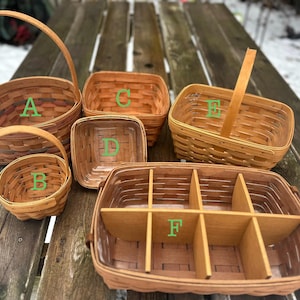 Puede incluir: Una colección de seis cestas de madera tejida de varias formas y tamaños. Las cestas son de tonos marrones y beige, algunas con asas. Están dispuestas sobre una superficie de madera envejecida, mostrando su encanto rústico.