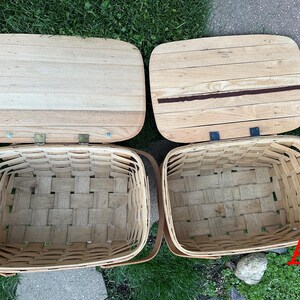 May include: Two rectangular picnic baskets with wooden lids. The baskets are woven with light brown strips, and the lids are made of light-colored wood. One lid has a dark brown stripe. The baskets are open, revealing their empty interiors.