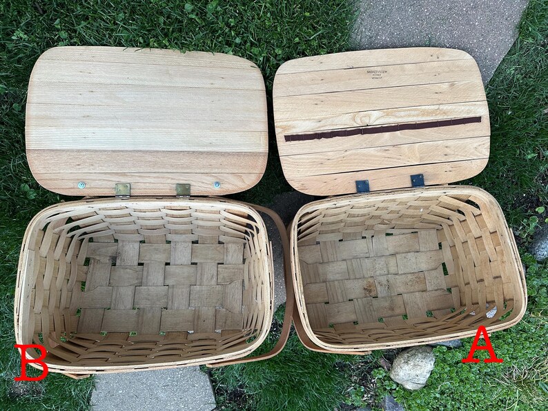 May include: Two rectangular picnic baskets with wooden lids. The baskets are woven with light brown strips, and the lids are made of light-colored wood. One lid has a dark brown stripe. The baskets are open, revealing their empty interiors.