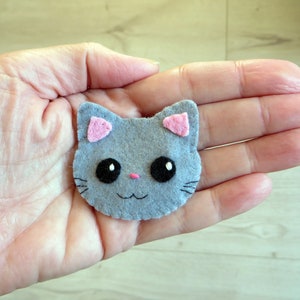 broche en feutrine, tête de chat gris avec de grands yeux noirs, nez rose, oreilles roses