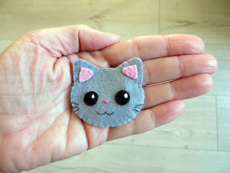 broche en feutrine, tête de chat gris avec de grands yeux noirs, nez rose, oreilles roses