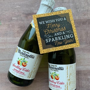 May include: Two green glass bottles of Martinelli's Sparkling Cider with a gold-glittered tag that reads "We wish you a Merry Christmas and a Sparkling New Year!". The bottles are 8.4 fl oz (250ml) each.