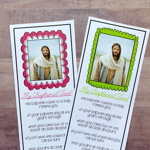 May include: Two pink and green cards with a white border and scalloped edges. Each card features a picture of Jesus in the center. The text on the cards reads "My Baptismal Towel" and includes a message about the significance of baptism.