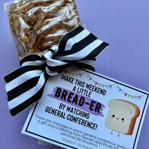 May include: A brown baked good wrapped in clear plastic, tied with a black and white striped ribbon. Attached is a white card with colorful bunting, a cartoon bread slice, and the text: MAKE THIS WEEKEND A LITTLE BREAD-ER BY WATCHING GENERAL CONFERENCE!