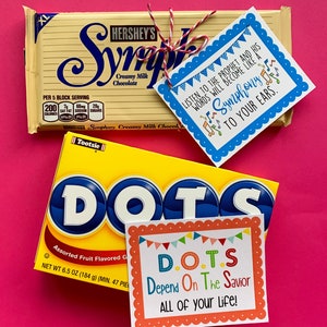 May include: Two candy bars with inspirational messages attached. The first is a Hershey's Symphony bar with a blue tag that says "Listen to the prophet and his words will become like a symphony to your ears." The second is a Tootsie Roll Dots candy bar with a colorful tag that says "D.O.T.S. Depend On The Savior ALL OF your life!"