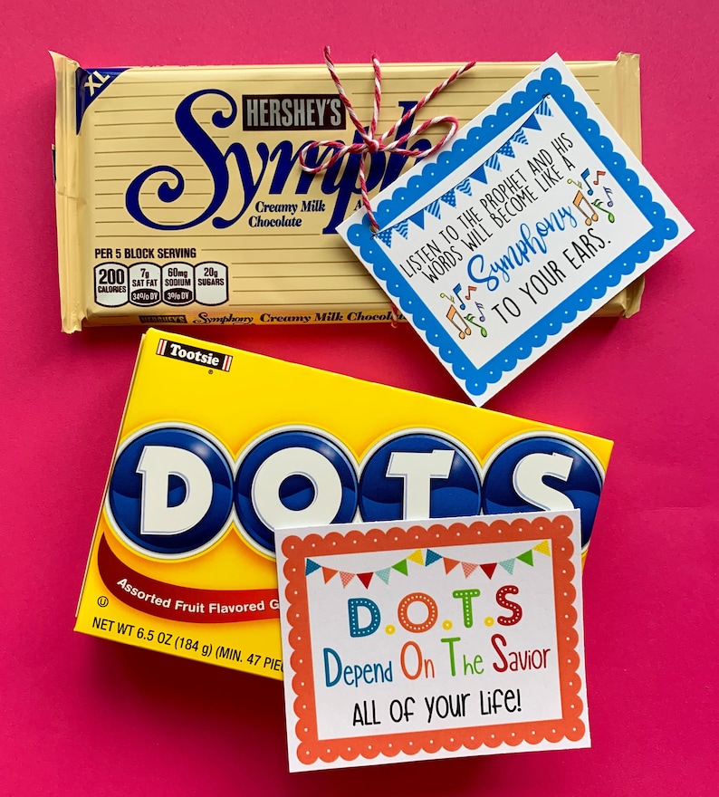 May include: Two candy bars with inspirational messages attached. The first is a Hershey's Symphony bar with a blue tag that says "Listen to the prophet and his words will become like a symphony to your ears." The second is a Tootsie Roll Dots candy bar with a colorful tag that says "D.O.T.S. Depend On The Savior ALL OF your life!"