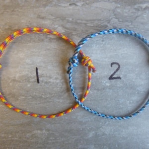 May include: Two friendship bracelets, one with a blue and white striped pattern and the other with a red, yellow, and orange striped pattern.