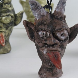 Peut inclure: Une figurine en c&eacute;ramique brune repr&eacute;sentant un diable avec des cornes, une longue langue et une expression espi&egrave;gle. La figurine est peinte avec des d&eacute;tails noirs et blancs et a une surface textur&eacute;e.