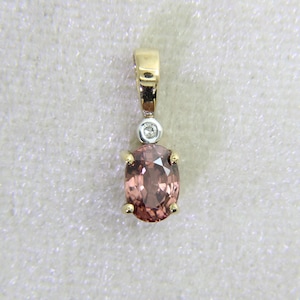 May include: A gold pendant with a pink oval gemstone. The pendant has a small diamond accent and a gold bail. The gemstone is set in a gold bezel with four prongs.