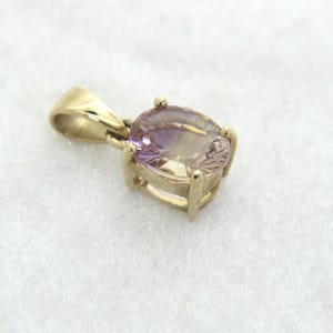 May include: A gold pendant featuring an oval-cut, light purple gemstone. The gemstone is set in a gold bezel setting with four prongs. The pendant has a gold bail for attaching to a chain. The overall design is simple and elegant.