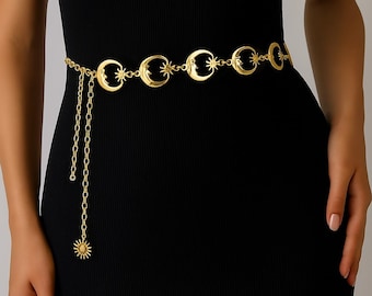 May include: Gold-toned waist belt featuring crescent moons and stars. The belt has a chain with a sun pendant. The belt is worn over a black dress. The belt is a stylish accessory.