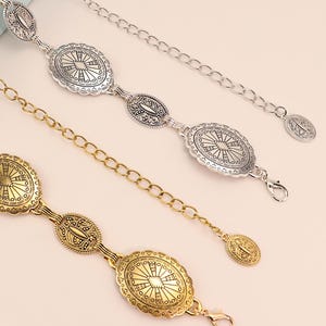 May include: Three decorative belts with oval-shaped medallions and chain links. One belt is silver, and the other two are gold. The medallions feature intricate sunburst and floral patterns. Each belt has a clasp closure.