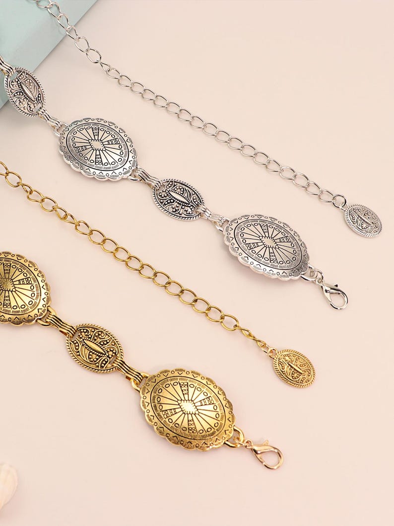 May include: Three decorative belts with oval-shaped medallions and chain links. One belt is silver, and the other two are gold. The medallions feature intricate sunburst and floral patterns. Each belt has a clasp closure.