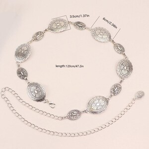 May include: Silver metal belt featuring oval and oblong decorative elements. The belt is 120cm long, with oval pieces measuring 6cm. The belt has a chain extension and a clasp closure. The decorative elements have a detailed, engraved design.