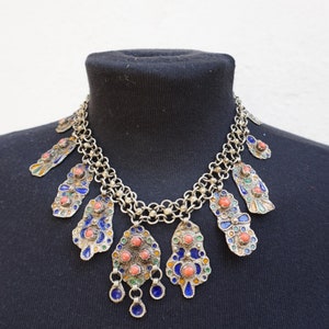 May include: A silver necklace with a chain and multiple pendants. The pendants are decorated with blue, green, and orange enamel and coral beads.