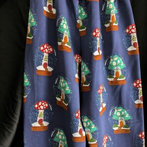 May include: Blue pants with a repeating pattern of mushroom-shaped snow globes. The mushrooms have red and green caps, with small houses inside the globes. The waistband is a solid mauve color.