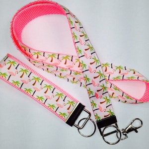 May include: Pink and white lanyard with a flamingo and palm tree pattern. The lanyard has a detachable key ring.