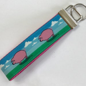 May include: A pink and green key chain with a blue background and two cartoon pigs. The key chain has a silver metal key ring.