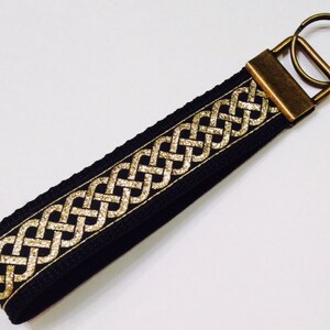 May include: Black and gold key chain with a Celtic knot design. The key chain has a brass key ring.