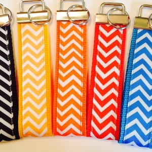 May include: Five keychains with chevron patterns. The keychains are black and white, orange and white, red and white, orange and white, and blue and white.