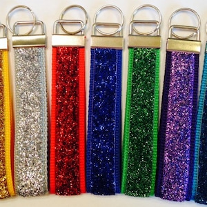 May include: Eight keychains with glitter fabric and a silver key ring. The keychains are in the colors gold, silver, red, blue, green, purple, and two shades of blue.