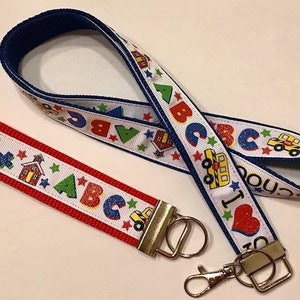 May include: A red and white ribbon with the letters ABC and stars, attached to a blue and white ribbon with the words "I Love School" and school bus and schoolhouse graphics. The ribbons are attached to a silver key chain.