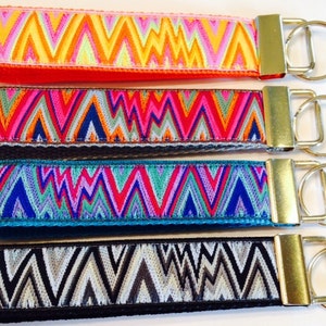 May include: Set of four colorful keychains with a geometric chevron pattern. Each keychain has a gold metal key ring.