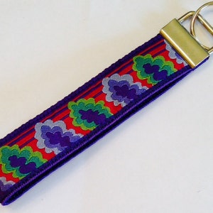 May include: Purple key chain with a red, white, and green floral pattern. The key chain has a silver key ring.