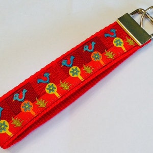 May include: Red key chain with a colorful pattern of birds and flowers. The key chain has a silver metal key ring.
