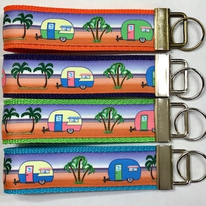 May include: Four colorful keychains with a retro camper design. Each keychain features a different color scheme with a camper, palm trees, and a beach scene. The keychains are attached to silver key rings.
