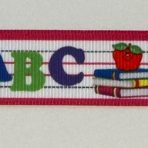 May include: White ribbon with a red border featuring the letters ABC, numbers 123, and illustrations of an apple on books and a worm wearing glasses. The ribbon is designed for educational or school-themed crafts.