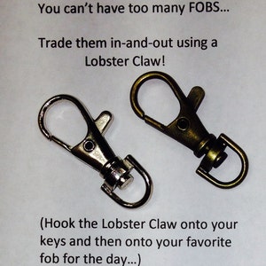 May include: Two keychains, one silver and one bronze, with lobster claw clasps. The text "You can't have too many FOBS... Trade them in-and-out using a Lobster Claw! (Hook the Lobster Claw onto your keys and then onto your favorite fob for the day...)" is written below the keychains.