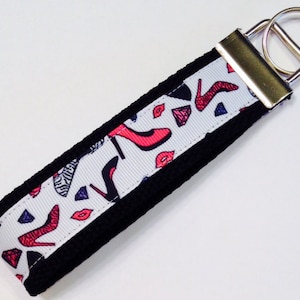 May include: A white and black key chain with a silver key ring. The white part of the key chain has a pattern of red high heels, lips, and diamonds.